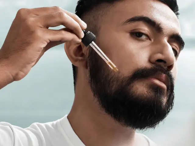 black man holding a pipette with a beard oil