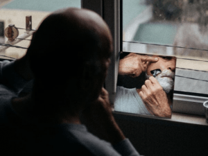 Man shaving while facing the window and mirror