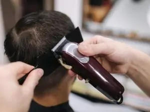 professional hairdresser using a hair clipper to a young man